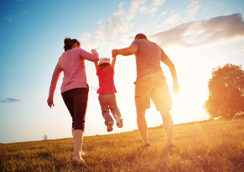 A family running hand-in-hand through a sunny field.