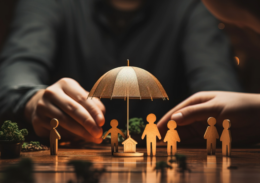 Wooden figures sheltered by an umbrella, symbolizing protection.