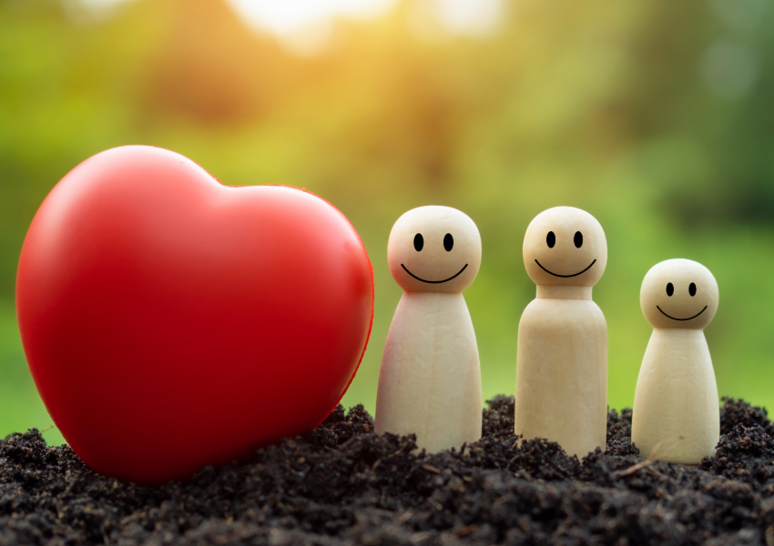 Smiling wooden figures with a large red heart on soil.