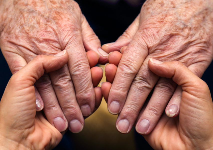 Elderly hands holding younger hands in a tender gesture.