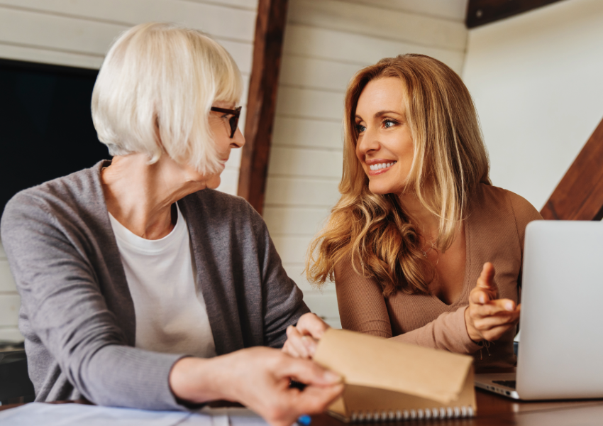 Smiling woman consulting with elderly mother over laptop.