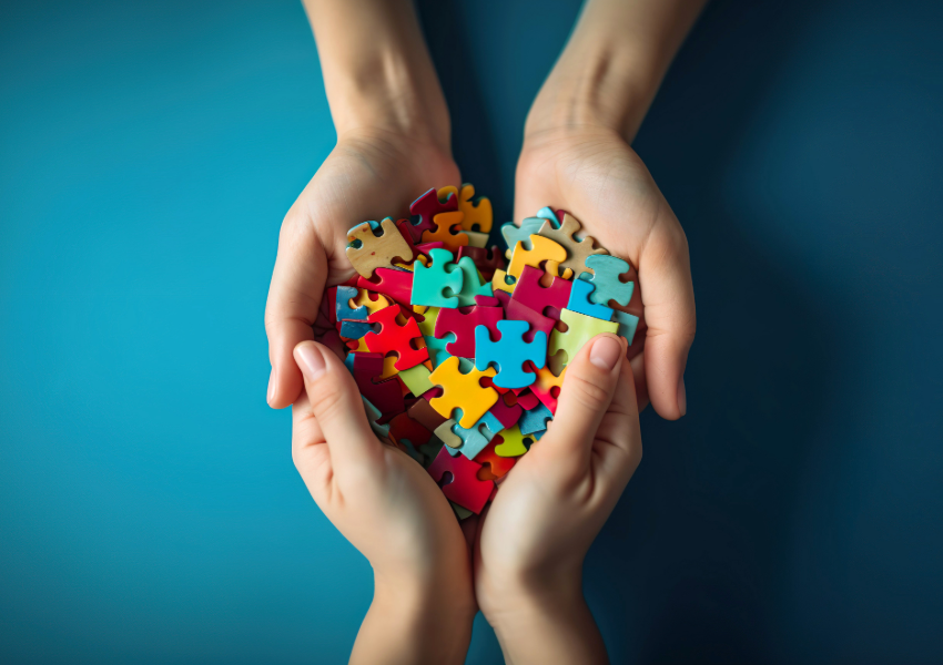 Hands holding a heart made of colorful puzzle pieces.