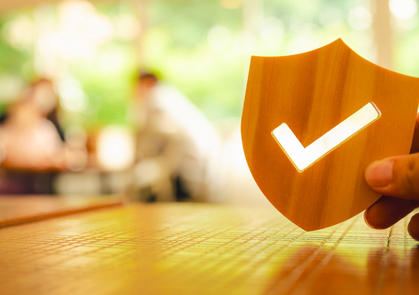 Hand holding a wooden shield with a checkmark, symbolizing assured protection.